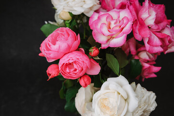 Pink and white roses bloom in a rich floral bouquet against a dark backdrop.