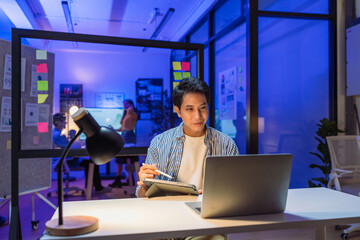 modern office late at night focused young business person exemplifies dedication productivity, diligently viewing his laptop computer utilizing digital tablet to drive strategic initiatives