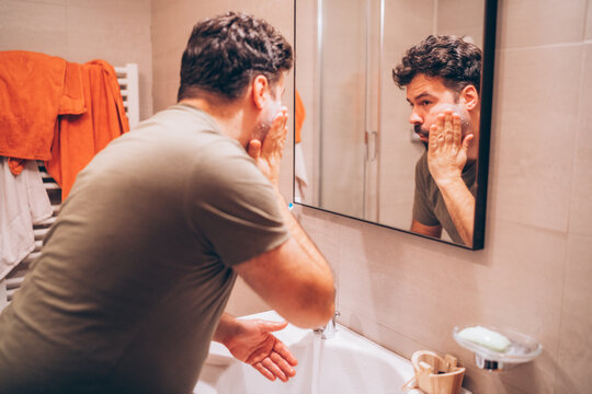 Man washing his face in a modern bathroom during morning skincare routine - Powered by Adobe