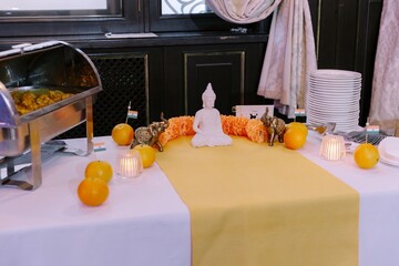 Buffet table setting with an Indian theme, featuring a white Buddha statue, golden elephant figurines, and oranges, with a chafing dish of curry on the side