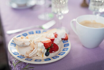 Dessert with coffee. Cake of meringue with strawberries on a plate and cup of coffee on a table. Homemade sweet food for eating. Close up. Violet background.