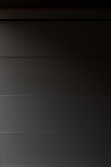 Porte de garage grise anthracite installée par un professionnel, encadrée par un mur en pierre beige et un sol en macadam, entre modernité et authenticité.