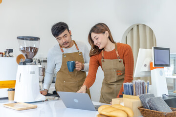 Happy couple entrepreneur reviewing sales report on laptop inside small business cafe, smiling baristas celebrating turnover growth, representing success, digital management, and startup confidence