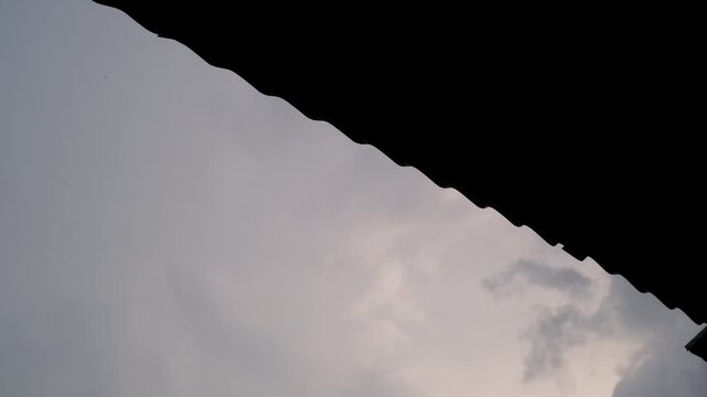 Low-angle footage of rainwater dripping from the edge of a zinc roof. Videography of water droplets during heavy rain in the yard. Relaxing ambience in 4K resolution footage.