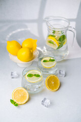 Lemon water with mint leaves and ice served in glass with fresh citrus on light background
