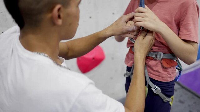 Instructor assisting young boy with safety harness for indoor rock climbing, teaching safety methods and belaying techniques at a climbing gym, fostering learning and training