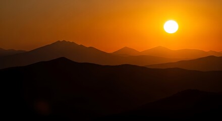 Obraz premium Vibrant sunset over silhouetted mountain ranges casting a warm orange glow across the sky