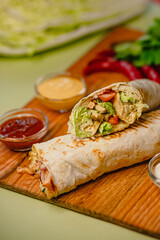 Delicious chicken wrap with lettuce and tomato on wooden board