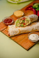 Fresh chicken wrap with lettuce, tomato, sauces, and peppers on wooden board
