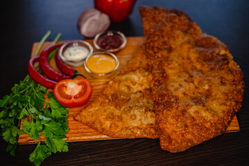 Crispy fried chebureki with dipping sauces, tomato, peppers, onion, and fresh herbs on wooden board