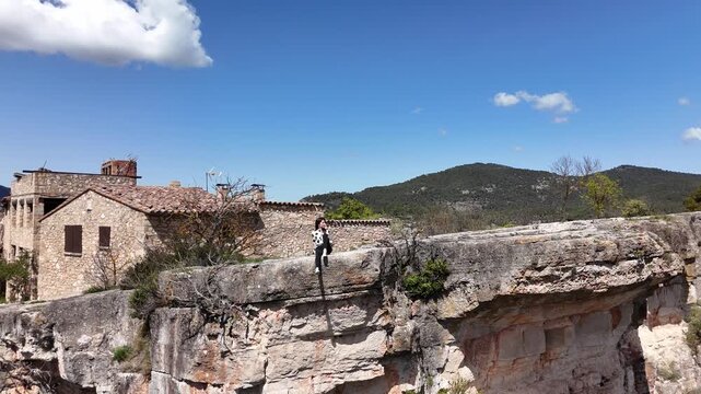 Joven sentada al borde del acantilado de Siurana, en Tarragona, Catalu&ntilde;a. El movimiento del dron revela una impresionante panor&aacute;mica del pueblo y el paisaje monta&ntilde;oso. libertad, naturaleza, viajes.