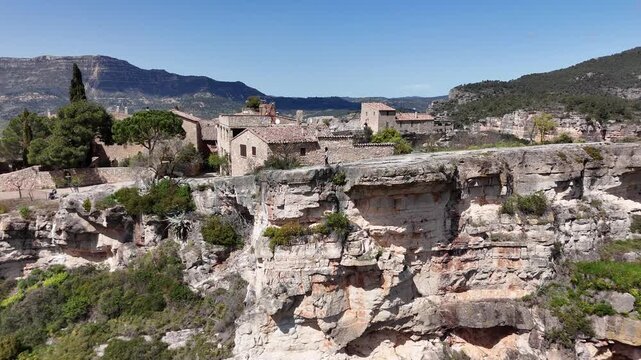 Joven sentada al borde del acantilado de Siurana, en Tarragona, Catalu&ntilde;a. El movimiento del dron revela una impresionante panor&aacute;mica del pueblo y el paisaje monta&ntilde;oso. libertad, naturaleza, viajes.