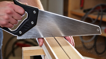 Carpenter at work with hand saw cutting wood for construction and woodworking projects