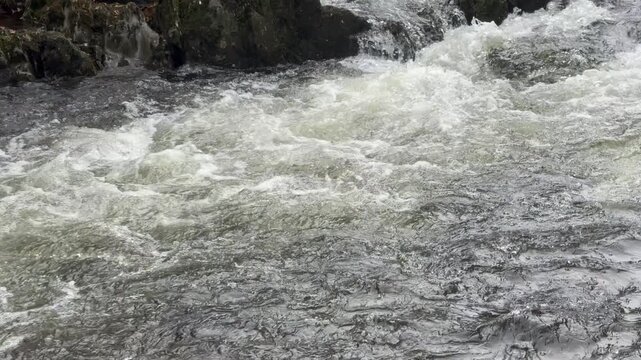 Slow motion of watcher rushing down a a large river with rocks and boulders UK 4K