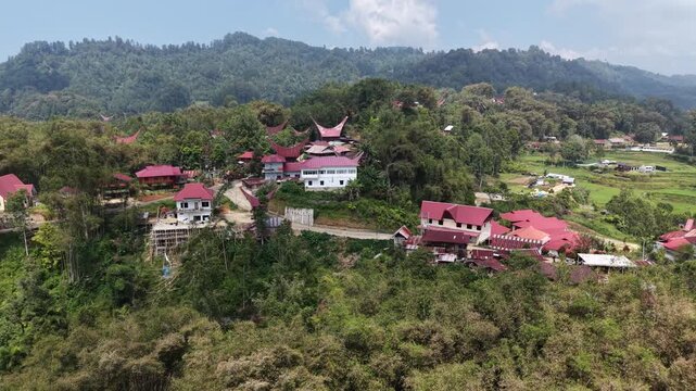 Aerial view of traditional Tongkonan houses with curved roofs on a hillside in Tana Toraja, Indonesia, surrounded by mountains and clouds.	
