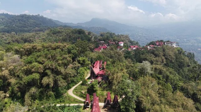 Aerial view of traditional Tongkonan houses with curved roofs on a hillside in Tana Toraja, Indonesia, surrounded by mountains and clouds.	
