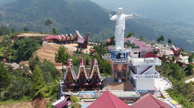 Massive statue of Jesus Christ with outstretched arms overlooking the lush mountainous landscape in Tana Toraja, Indonesia.
