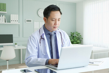 Portrait of asian senior doctor sitting in medical office while using laptop computer and checking time of appointment.