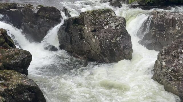 Slow motion of watcher rushing down a a large river with rocks and boulders UK 4K