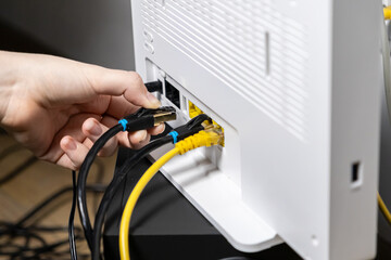 Human hand plugging a black Ethernet cable into a white internet router, establishing a secure network connection for modern digital technology setup