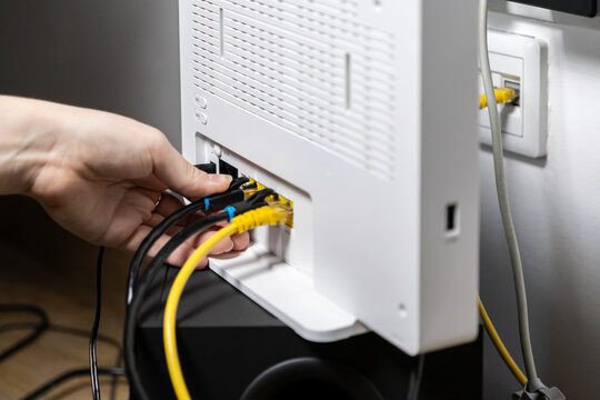 Person's hand skillfully plugs yellow Ethernet and black power cables into a white Wi-Fi router, setting up reliable home internet connection