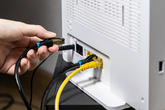 Person's hand connecting a black Ethernet cable into a white wireless internet router, symbolizing network setup, reliable broadband, and home technology
