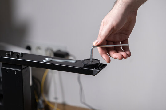 Skilled hand adjusting a furniture leveling foot with an Allen key on a modern black metal desk frame, showcasing DIY assembly and home improvement