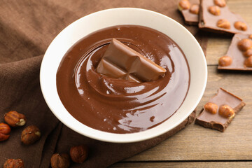 Melted chocolate and pieces with hazelnuts on wooden table, closeup