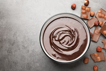 Melted chocolate in bowl, pieces and nuts on grey table, flat lay. Space for text