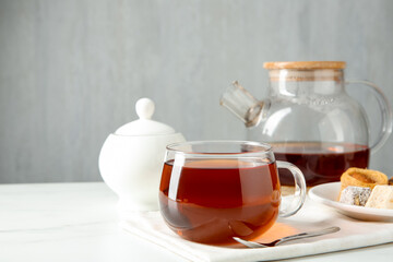 Tasty tea in glass cup, teaspoon, Turkish desserts, teapot and sugar bowl on white table against grey background, closeup. Space for text