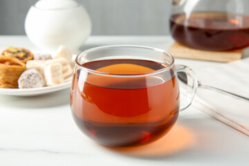 Tasty tea in glass cup on white table against grey background, closeup