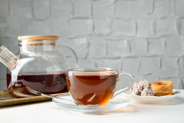 Tasty tea in glass cup, teapot and Turkish desserts on white table against grey textured background, closeup