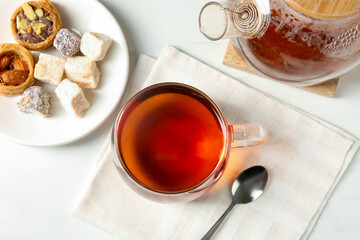 Tasty tea in glass cup, teaspoon, Turkish desserts and teapot on white table, flat lay