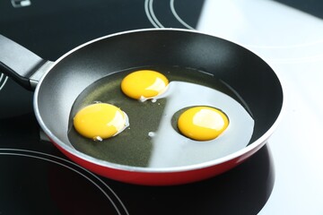 Frying pan with raw chicken eggs on cooktop in kitchen, closeup