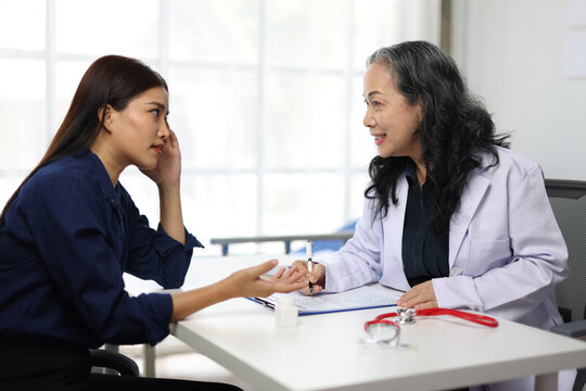 A young woman with a headache is consulting a senior doctor in a hospital. - Powered by Adobe