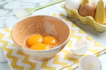 Raw eggs, yolks and brush on white marble table, closeup
