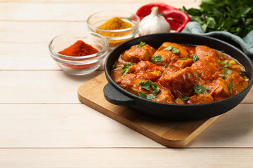 Chicken tikka masala with spices on light wooden table, closeup. Space for text
