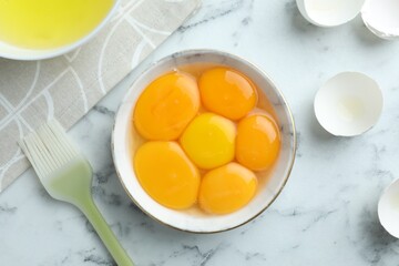 Egg yolks, whites and brush on white marble table, flat lay