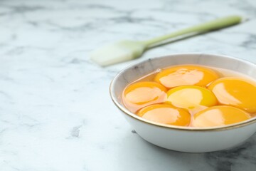 Egg yolks in bowl and brush on white marble table, closeup. Space for text
