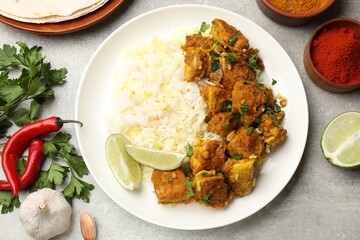 Delicious chicken tikka masala with rice, parsley, lime and spices on grey textured table, flat lay