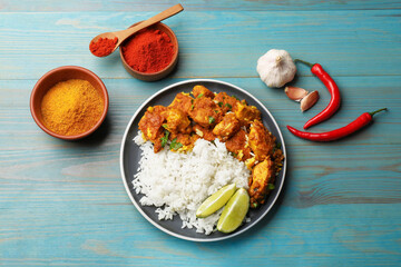 Delicious chicken tikka masala with rice, parsley, lime and spices on light blue wooden table, flat lay