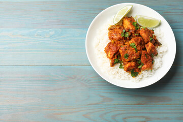 Delicious chicken tikka masala with rice, parsley and lime on light blue wooden table, top view. Space for text