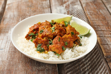 Delicious chicken tikka masala with rice, parsley and lime on color wooden table, closeup