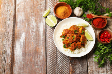 Delicious chicken tikka masala with rice, parsley, lime and spices on color wooden table, flat lay. Space for text