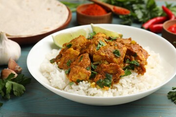 Delicious chicken tikka masala with rice, parsley, lime and spices on light blue wooden table, closeup