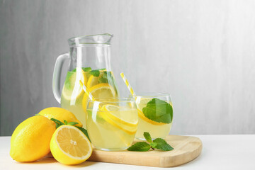 Fresh lemonade in glasses, jug, lemons and mint on white table, closeup. Space for text
