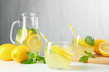 Fresh lemonade in glasses, jug, lemons and mint on white table, closeup