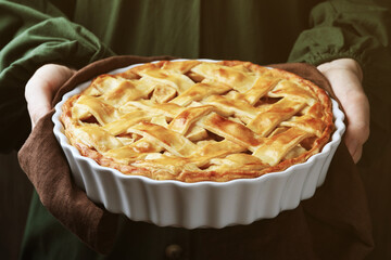 Woman with baking dish of delicious homemade apple pie against dark background, closeup