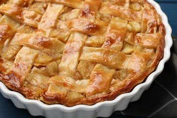 Delicious homemade apple pie in baking dish on blue table, closeup