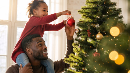 A young African American girl on her father's shoulders decorating a Christmas tree. Happy family enjoying holiday traditions together at home